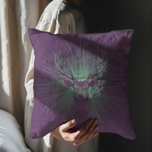 A pillow cover with a bold stag's head emerging from an ethereal burst of mint green rays against deep purple fabric. Delicate starbursts scatter around the deer, creating a celestial effect.